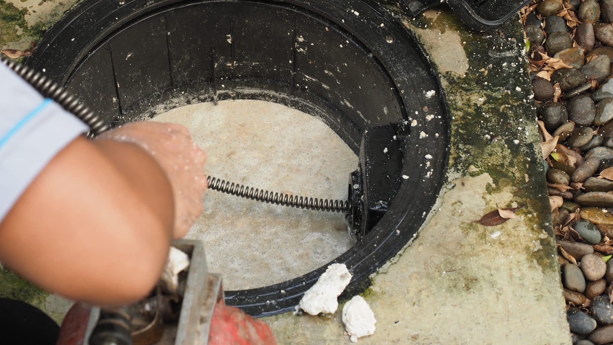 Professional plumber using an auger to unclog a grease trap, highlighting the importance of timely grease trap cleaning.