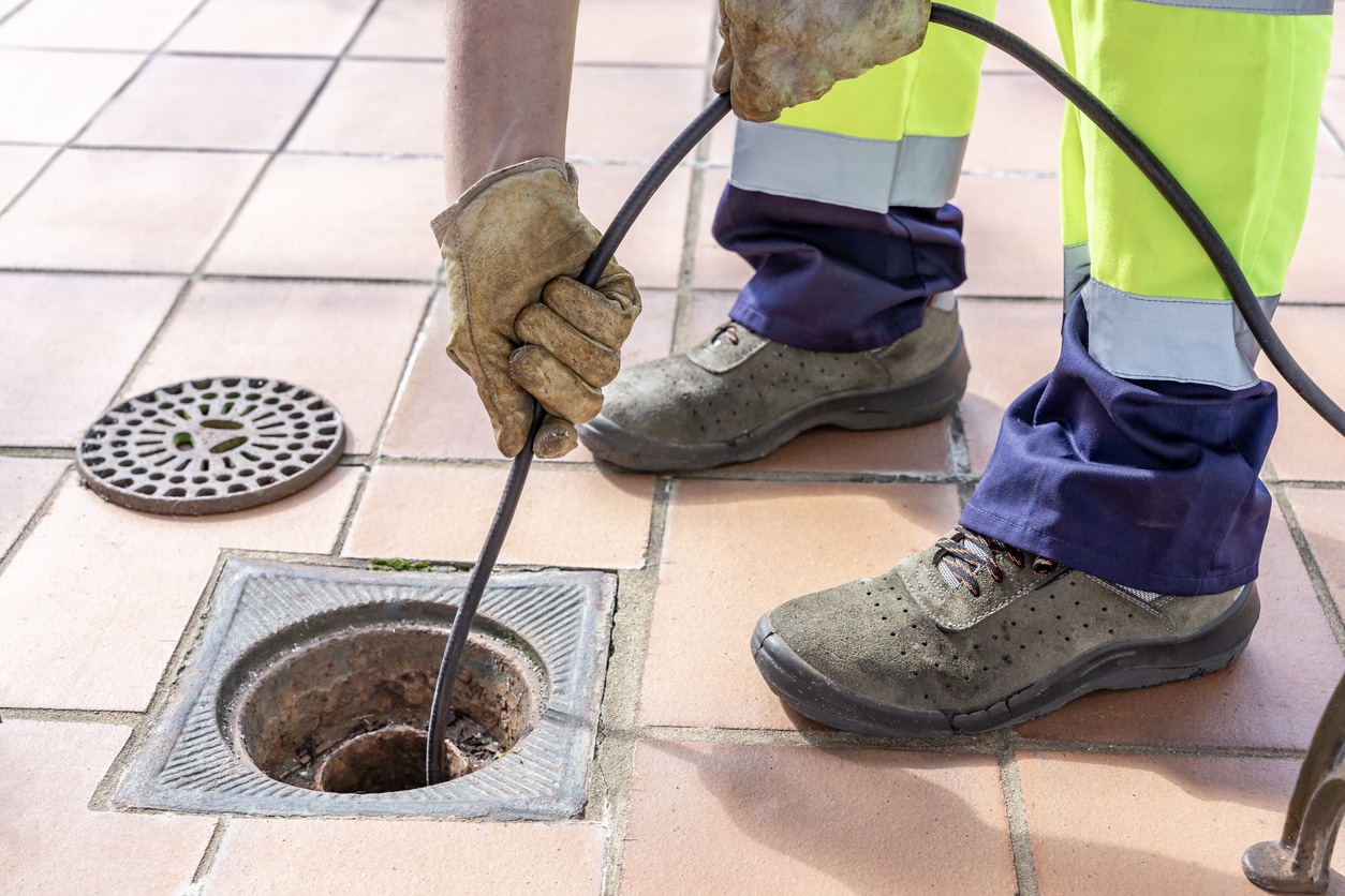 A professional from PowerVac of Michigan in high-visibility gear uses a drain snake to clear a clogged floor drain.